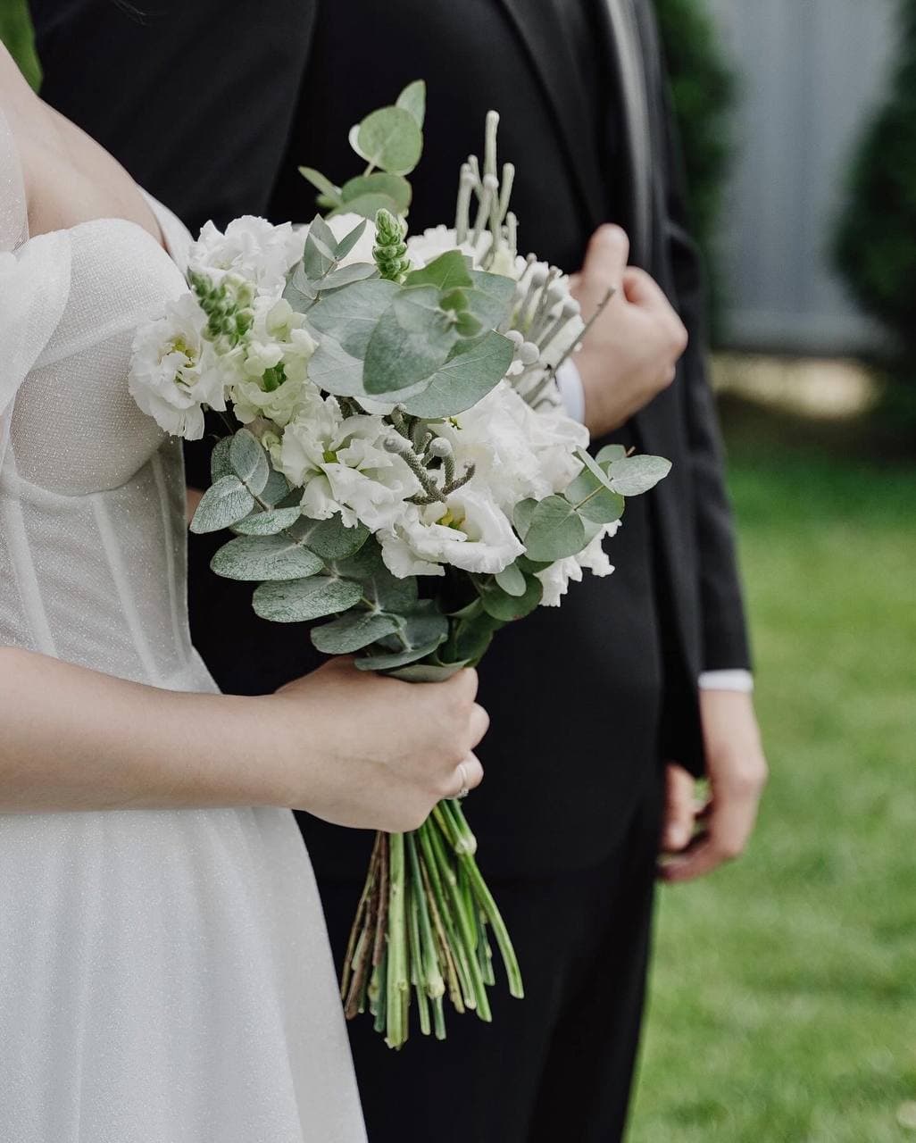 Couple embracing, the bride holding a white and eucalyptus bouquet